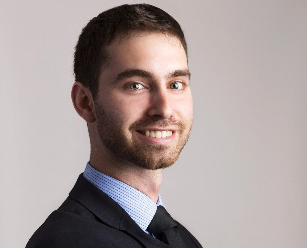 Smiling man with short dark hair, wearing a suit and tie, in a professional headshot.